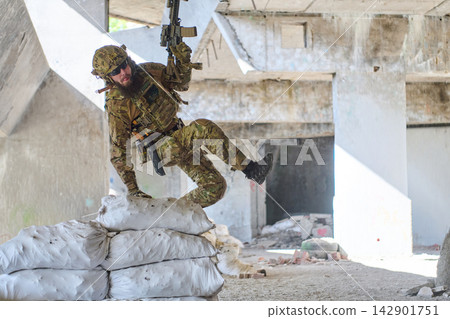 Soldier In Camouflage Tactical Gear Leaping Over Sandbags With Rifle During Urban Combat Training Soldier In Camouflage Tactical Gear Leaping Over Sandbags With Rifle During Urban Combat Training 142901751