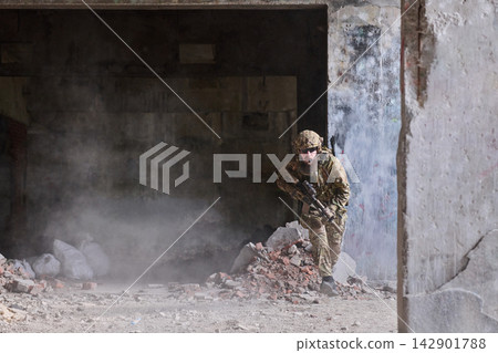Soldier In Tactical Gear Moving Through Urban Ruins With Rifle During Combat Training Operation Soldier In Tactical Gear Moving Through Urban Ruins With Rifle During Combat Training Operation 142901788