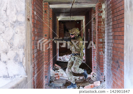 Soldier in Tactical Gear Clearing Rubble-Filled Corridor During Urban Combat Training Exercise Soldier in Tactical Gear Clearing Rubble-Filled Corridor During Urban Combat Training Exercise 142901847