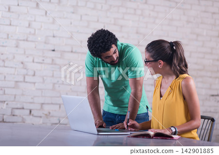 Young professionals collaborate in a casual coworking space over laptop and notebook Young professionals collaborate in a casual coworking space over laptop and notebook 142901885