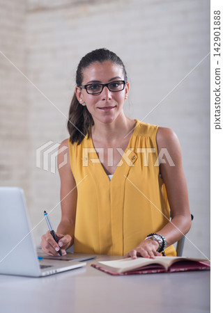 Young female entrepreneur working in a startup coworking office with laptop and notebook Young female entrepreneur working in a startup coworking office with laptop and notebook 142901888