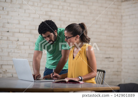 Young Middle Eastern coworkers collaborating on laptop and notebook in a creative startup office 142901889