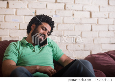 Young Middle Eastern entrepreneur in a casual coworking startup space smiling while talking on phone Young Middle Eastern entrepreneur in a casual coworking startup space smiling while talking on phone 142901904