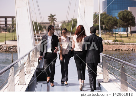 Business colleagues walking together across a modern pedestrian bridge in a city waterfront setting Business colleagues walking together across a modern pedestrian bridge in a city waterfront setting 142901918