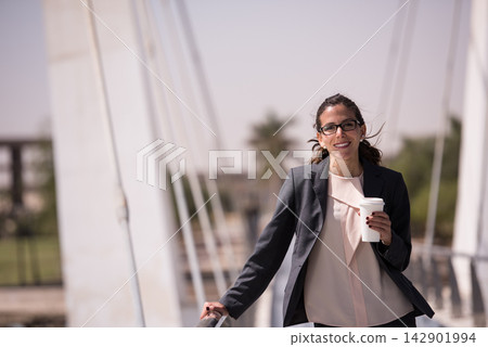 Businesswoman smiling with coffee on a bridge in a modern city, casual professional portrait outdoors Businesswoman smiling with coffee on a bridge in a modern city, casual professional portrait outdoors 142901994