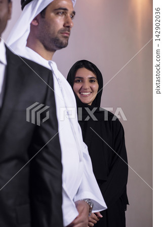 Emirati business team with smiling woman in abaya standing behind colleagues at corporate event Emirati business team with smiling woman in abaya standing behind colleagues at corporate event 142902036
