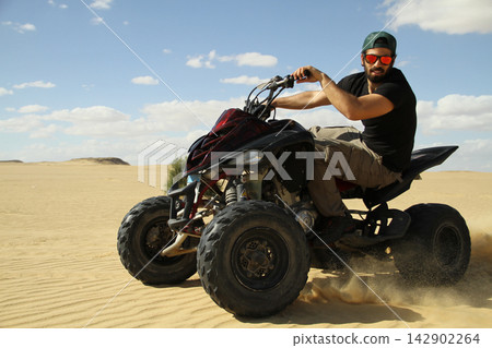 Young quad bike rider doing wheelie in desert 142902264