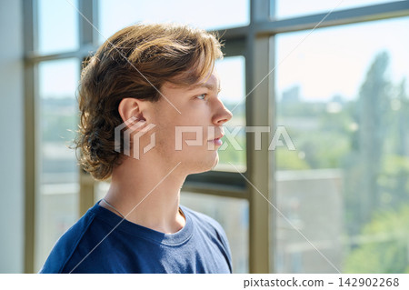 Side view profile portrait of handsome young man looking up near large window 142902268