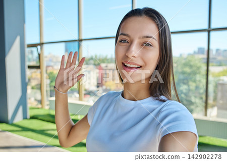 Young smiling female student making selfie video call and waving hand Young smiling female student making selfie video call and waving hand 142902278