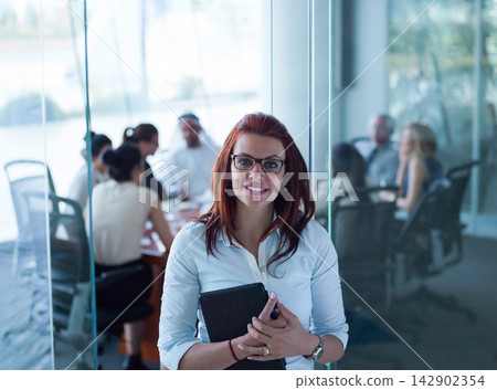 Confident Middle Eastern businesswoman smiling in modern corporate meeting room with startup team behind glass Confident Middle Eastern businesswoman smiling in modern corporate meeting room with startup team behind glass 142902354