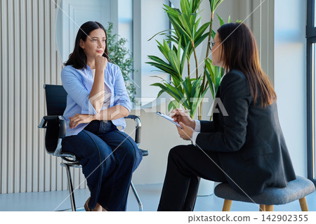 Young thoughtful woman sitting at therapy session talking with psychologist Young thoughtful woman sitting at therapy session talking with psychologist 142902355