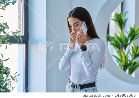 Shocked young woman covering mouth while speaking on smartphone 142902366