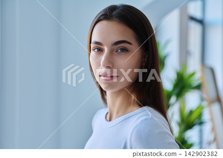 Side view portrait of smiling young woman looking at camera in modern interior Side view portrait of smiling young woman looking at camera in modern interior 142902382