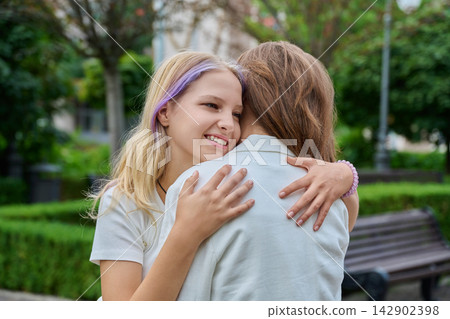 Happy teenage girl hugging mother warmly standing in park Happy teenage girl hugging mother warmly standing in park 142902398