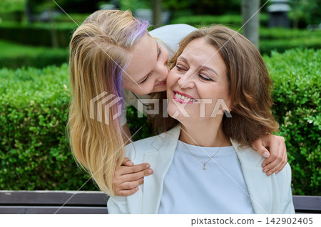 Teenage daughter kissing happy mother on cheek outdoors in park Teenage daughter kissing happy mother on cheek outdoors in park 142902405
