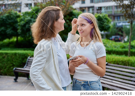 Caring mother touching hair of her teenage daughter outdoors in park Caring mother touching hair of her teenage daughter outdoors in park 142902418
