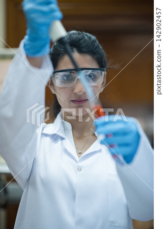Middle Eastern female doctor performing precise blood testing in clinical laboratory with pipette and safety goggles Middle Eastern female doctor performing precise blood testing in clinical laboratory with pipette and safety goggles 142902457