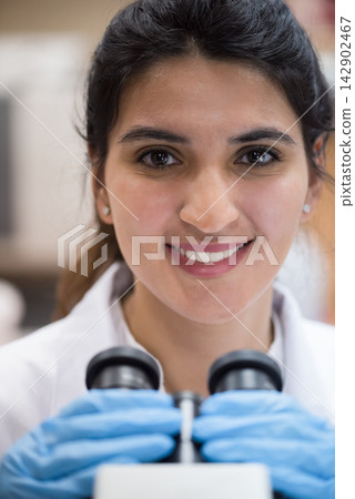 Middle Eastern female medical technician in lab smiling while using microscope for blood testing and diagnostics Middle Eastern female medical technician in lab smiling while using microscope for blood testing and diagnostics 142902467