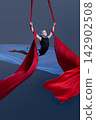 Teen aerialist opening arms between flowing silks 142902508