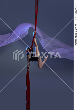 Teen girl holding dynamic pose above red silks 142902515