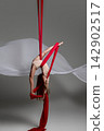 Teen girl inverted on red aerial silks 142902517
