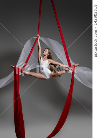 Teen girl performing split on red aerial silks Teen girl performing split on red aerial silks 142902519