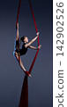 Teen aerialist climbing red silks on dark blue background 142902526