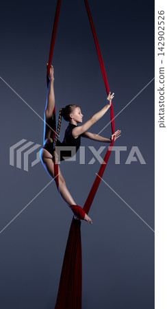 Teen aerialist climbing red silks on dark blue background Teen aerialist climbing red silks on dark blue background 142902526