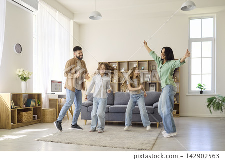 Cheerful parents and daughters dancing in cozy living room at home together Cheerful parents and daughters dancing in cozy living room at home together 142902563