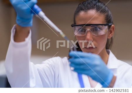 Female laboratory technician carefully pipetting blood sample in clinical research lab Female laboratory technician carefully pipetting blood sample in clinical research lab 142902581