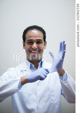 Male doctor putting on gloves in a clinical lab while preparing for blood testing and patient care Male doctor putting on gloves in a clinical lab while preparing for blood testing and patient care 142902599