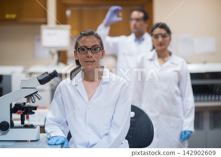 Young medical professionals in lab coats conducting blood testing and clinical research with microscope Young medical professionals in lab coats conducting blood testing and clinical research with microscope 142902609
