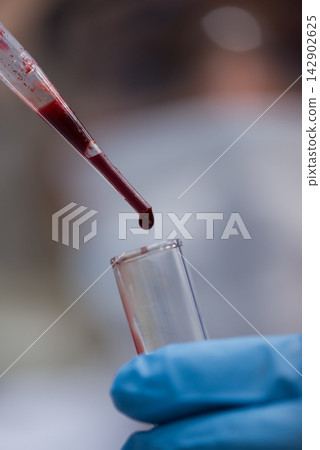 Young lab technician dropping a blood sample into a test tube during clinical testing procedure Young lab technician dropping a blood sample into a test tube during clinical testing procedure 142902625