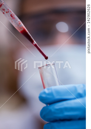 Young medical technician dropping blood sample into test tube in clinical laboratory with gloved hands Young medical technician dropping blood sample into test tube in clinical laboratory with gloved hands 142902626