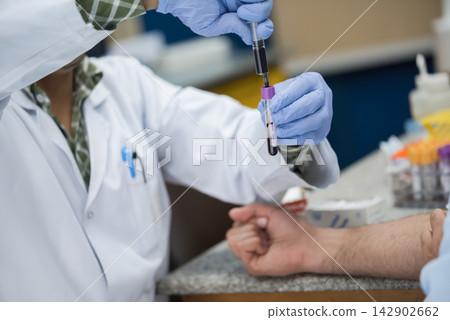 Middle Eastern medical team drawing blood sample in clinical lab while technician handles vial and syringe Middle Eastern medical team drawing blood sample in clinical lab while technician handles vial and syringe 142902662