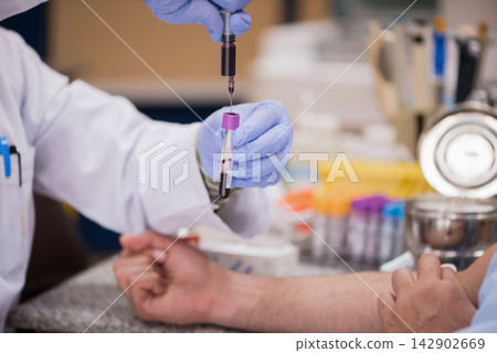 Young medical technician drawing blood sample in clinical laboratory while doctor prepares vial and syringe 142902669