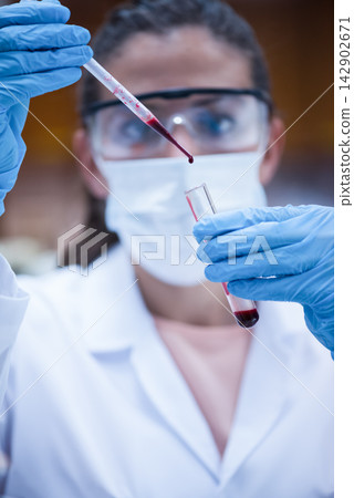 Middle Eastern female doctor in lab wearing mask and gloves testing a blood sample with a pipette Middle Eastern female doctor in lab wearing mask and gloves testing a blood sample with a pipette 142902671