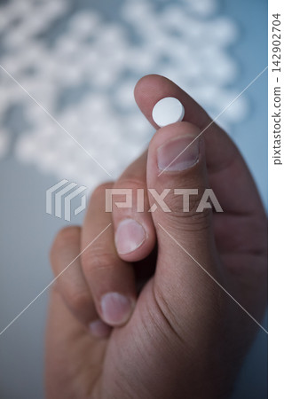 Medical professional holding a white tablet between fingers in clinical healthcare setting Medical professional holding a white tablet between fingers in clinical healthcare setting 142902704