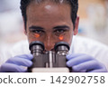 Young Middle Eastern lab technician examining blood sample under microscope in clinical medical laboratory 142902758