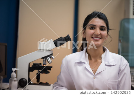 Young female doctor and medical technician smiling in a clinical blood testing laboratory with microscope Young female doctor and medical technician smiling in a clinical blood testing laboratory with microscope 142902925