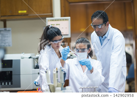 Young medical team performing blood testing in a clinical laboratory with protective gear and supervision Young medical team performing blood testing in a clinical laboratory with protective gear and supervision 142902958