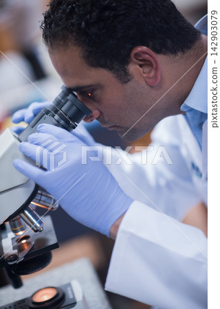 Young medical technician and doctor examining blood sample under microscope in clinical laboratory 142903079