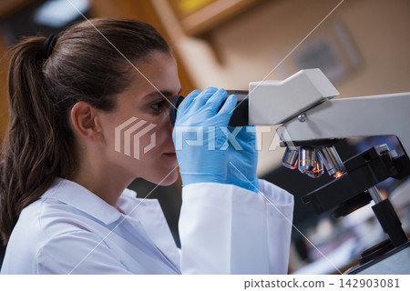 Young female medical technician examining blood samples under microscope in a clinical laboratory setting Young female medical technician examining blood samples under microscope in a clinical laboratory setting 142903081