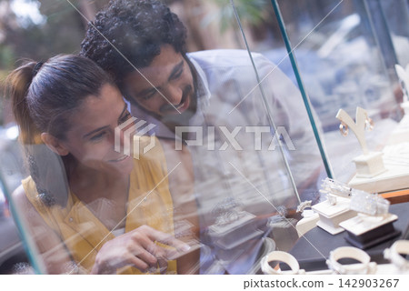 Middle Eastern couple shopping for a wedding ring together at a jewelry store display with smiles Middle Eastern couple shopping for a wedding ring together at a jewelry store display with smiles 142903267