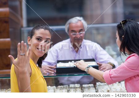 Happy couple and friends choosing an engagement ring at a jewelry store with smiling family support Happy couple and friends choosing an engagement ring at a jewelry store with smiling family support 142903330