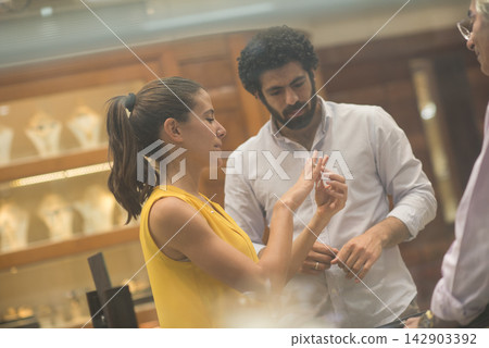 Middle Eastern couple choosing a wedding ring together in a jewelry store with friends and family Middle Eastern couple choosing a wedding ring together in a jewelry store with friends and family 142903392