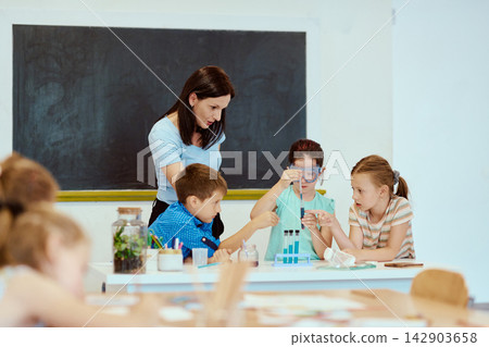 Teacher guiding students through a hands-on science experiment in a classroom with test tubes Teacher guiding students through a hands-on science experiment in a classroom with test tubes 142903658
