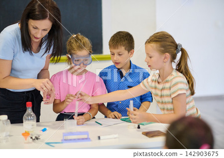 Teacher guiding children through a hands-on science experiment in a classroom activity Teacher guiding children through a hands-on science experiment in a classroom activity 142903675