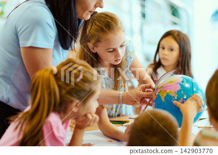 Teacher guiding children around a globe in a classroom during a hands-on geography lesson Teacher guiding children around a globe in a classroom during a hands-on geography lesson 142903770