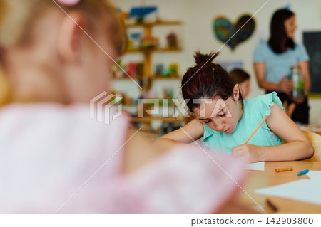 Young student concentrating on writing at a classroom table during a school art activity 142903800